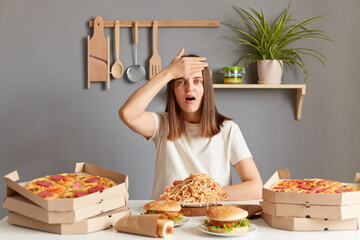 Portrait of sad despair woman with brown hair wearing white casual T-shirt sitting at table in...