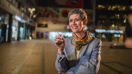 One caucasian senior woman stand in the city at night have a cigarette