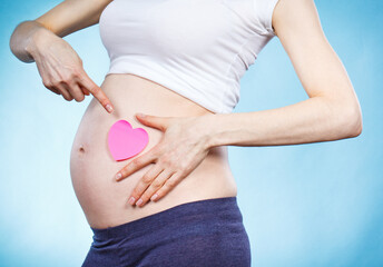 Woman in pregnant showing pink heart on her belly. Expecting for newborn. Extending family
