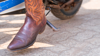woman's foot in cowboy boots removes the footboard of a motorcycle