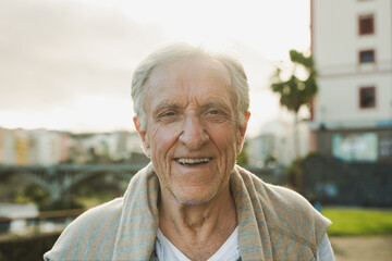 Happy senior man smiling on camera in the city with sunrise in the backround - Joyful elderly...