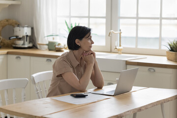 Serious concerned senior accountant woman thinking over financial risk, problems, mistake, overspending, sitting at table with calculator, laptop, document, looking away in deep thoughts