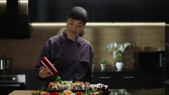 Slow-motion shot of a sushi master pouring sushi rolls with red tomato sauce in the kitchen. Sushi rolls making in process