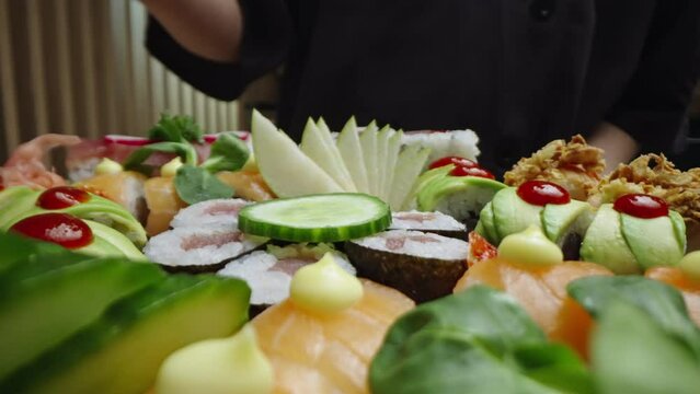 Panning up to down shot of lot of sushi bite size pieces decorated with greens served on tray ready to be eaten. Putting cucumber on sushi rolls in slow-motion. Close-up shot