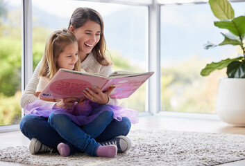 Get lost in the pages of a book. Shot of a young mother reading a book with her daughter at home.