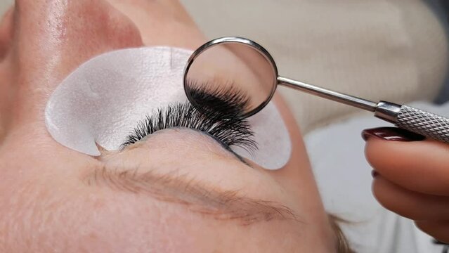 close up of eyelash Extensions in beauty salon after treatment, lash technician looking in lash mirror at result