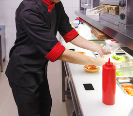Cook adding a ketchup on burger.