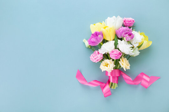 Bouquet of beautiful spring flowers with pink ribbon on pastel blue table for Happy mothers day. Flat lay.