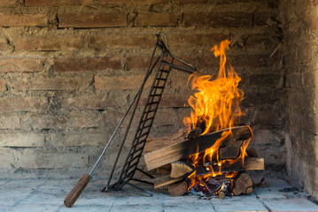 A fire in a brick oven with a metal tongs on it.