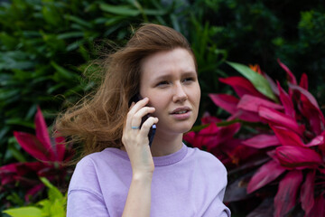 girl in the park or in nature uses a mobile phone, looks at the screen, smile and communication 