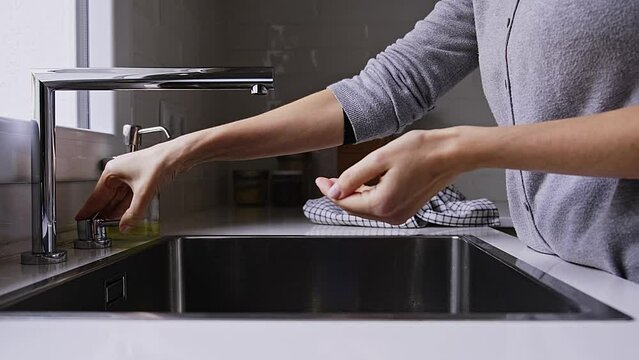 Unrecognizable woman washing hands with liquid soap in kitchen sink. 4k video.
