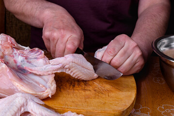 Female hands cutting raw chicken wings on wooden board in kitchen.