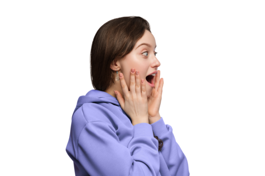 The girl is amazed in excitement on a light background, her hands on her cheeks, her mouth open.