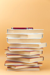 tower with stacked books, on top of them a pen of red color, the background in the image is orange