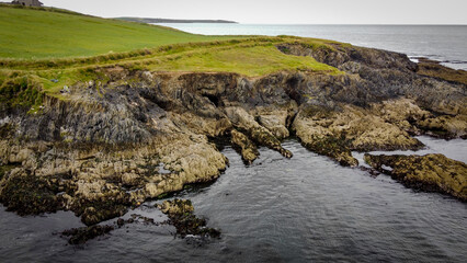 Naklejka na ściany i meble A picturesque rocky cape on the Atlantic coast of Ireland. Seaside landscape. Green grass field beside body of water