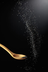 Grains of black sesame is poured with a wooden spoon.