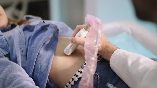 Close-up shot of a friendly young doctor performing ultrasound scan of a ten year old girl's abdomen in clinic