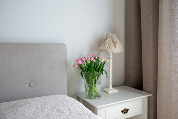 Beautiful pink tulips in vase on bedside table in bedroom