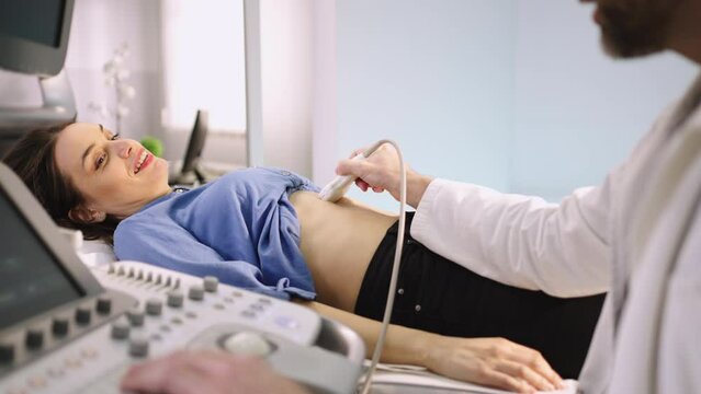 Young smiling woman having abdominal ultrasound scanning examination by her doctor in modern clinic