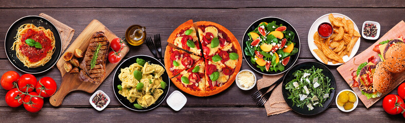 Table scene with various delicious foods. Overhead view on a dark wood banner background.