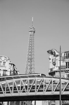 Paris cityscape with metro bridge (with passing train), Eiffel tower and French flag hanging out from the window of typical Parisian building. Black white historic photo