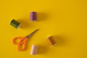 Pink, green, pink and brown threads along with tailor's scissors left on a yellow table