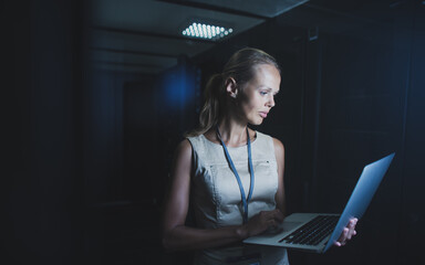 IT engineer standing before working server rack doing routine maintenance check and diagnostics using laptop