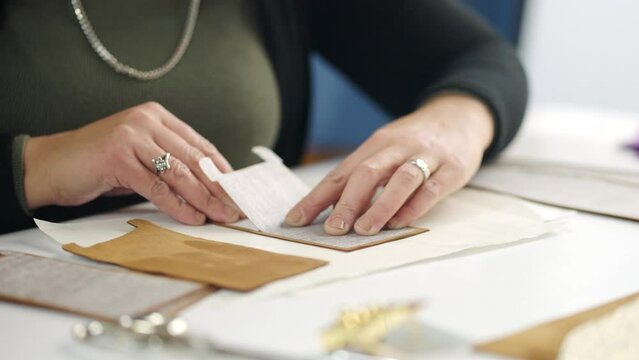 Woman tailor is applying glue on a leather parts on a work table in slow-motion. Workshop of a skinner during process sticking items of a leather accessories. Close-up