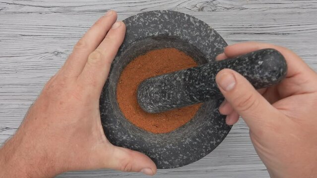 The top view of a pestle mixing finely grounded spices in the grey stone mortar