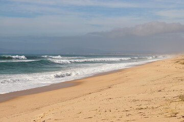 Fototapeta na wymiar Waves next to sandy beach on a sunny winter afternoon near Lisbon, Portugal.