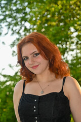 Naklejka premium A pretty young redhead woman smiling looking ahead in green nature