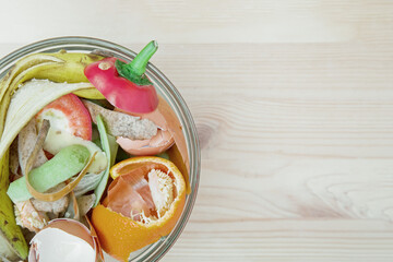 Compost from peelings of vegetables, fruits and egg shells in a glass bowl on a wooden table. The concept of waste-free consumption and eco-friendly lifestyle. View from above.