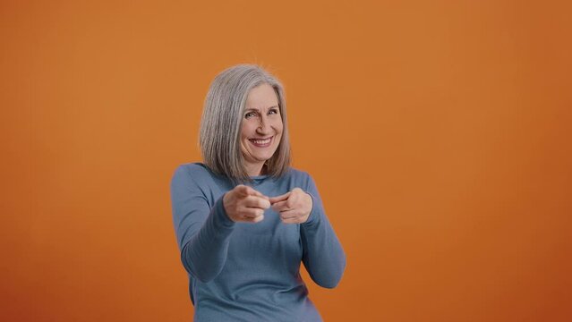 Joyful senior woman points fingers showing shot playfully