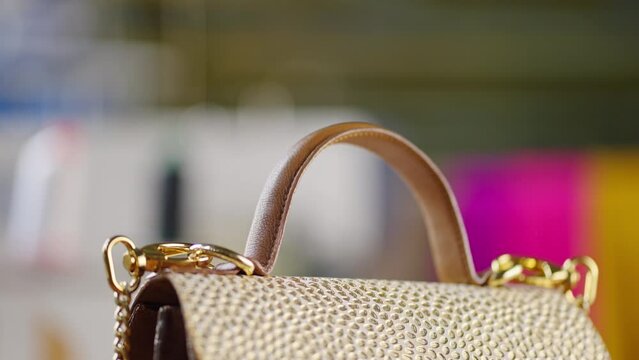 A close-up view of a brown leather female handbag with golden colored chain bracelet on a table