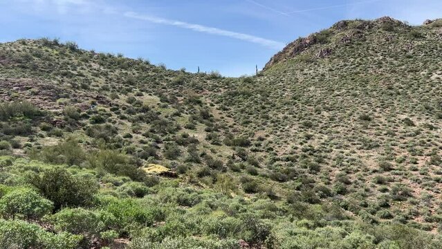 Distant hikers traverse a green desert valley as camera pans right