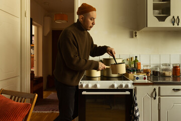 A caucasian man stirring in a saucepan preparing a meal in a kitchen at home.
