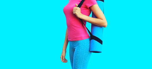 Sport and fitness concept - close up beautiful young woman in sportswear with yoga mat on blue background