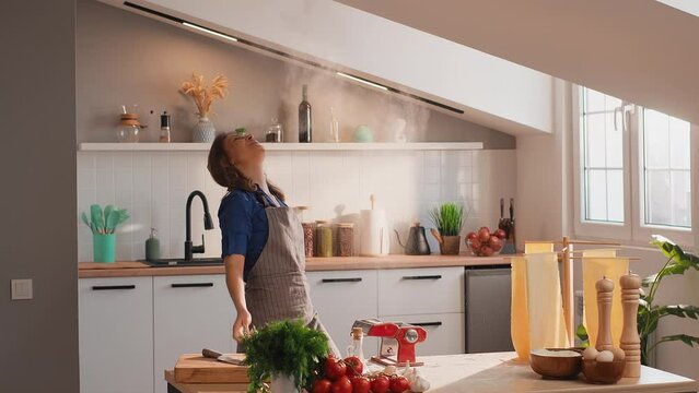 Young Happy Woman Having Fun In The Kitchen. A Woman Throwing Flour Up, Smiling And Dancing While Cooking Pasta At Home. Happy Holidays Concept