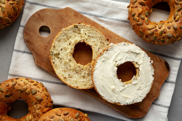 Homemade Whole Grain Bagel with Cream Cheese on a rustic wooden board, top view.