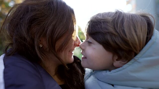 Mother and child doing eskimo kiss together. Mom and son caring and loving relationship standing outside in sunny day with sunlight flare