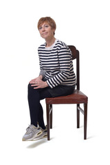 front side  view full length portrait of a woman in skirt, striped sweater and sneakers sitting on chair and legs crossed and looking at camera on white background