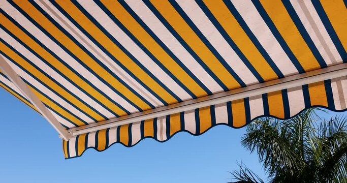striped retractable awning opens against blue sky