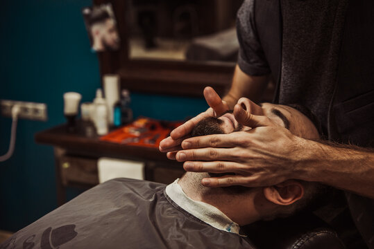 A professional barber cuts his beard to a young hipster man.