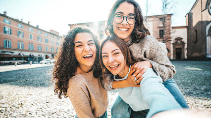 Three young women taking selfie picture with smart mobile phone outside - Girlfriends having fun on a sunny day out in city street - Life style concept with delightful females smiling at camera