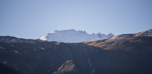 Panorama of mountain slopes with vegetation and trees yellowed in autumn and a rocky massif with snow, early autumn morning