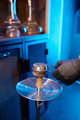 Closeup man making hookah putting hot coal cubes on tobacco bowl
