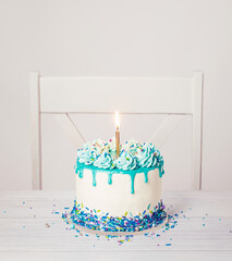 Birthday Cake with blue icing, ganache drip, sprinkles, and lit candle on a white background - 580157294