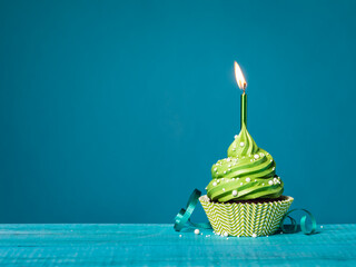Green cupcake with lit candle on a blue background.
