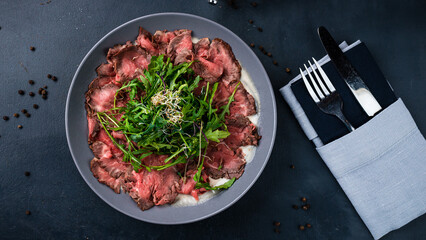 Appetizer of beef carpaccio with arugula, microgreens and sauce.
