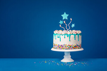 White birthday drip cake with teal ganache, star toppers and fun candles over dark blue background - obrazy, fototapety, plakaty